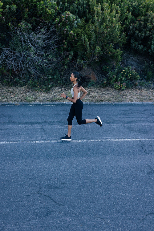 Side view of full length of slim female running on an abandoned road in a natural park. Woman practicing running outdoors.