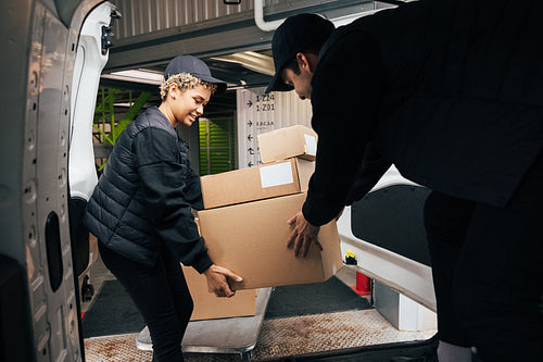 Two couriers stack cardboard boxes in a delivery van. Coworkers