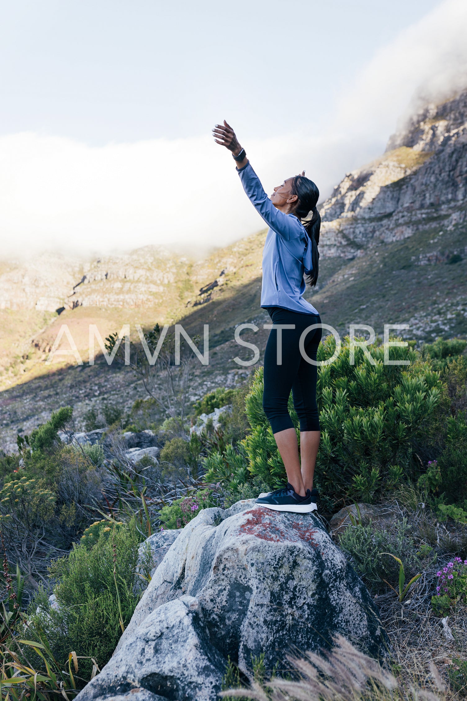 Full-length female trail runner enjoying nature. Young woman raising hands up while resting during trail run.