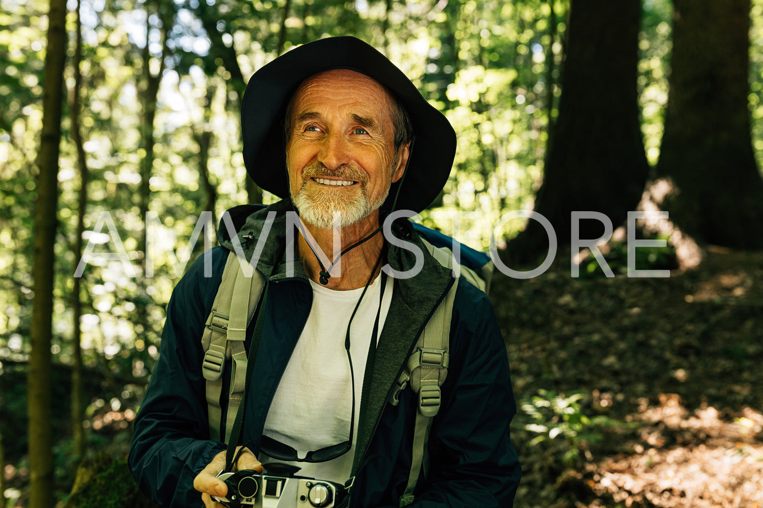 Cheerful senior male with a backpack and film camera taking a break during a forest walk