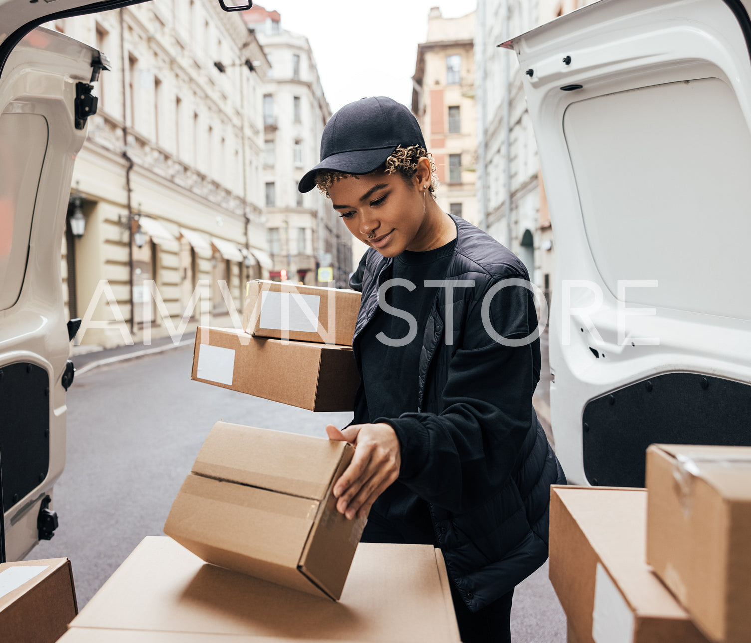 Young woman courier checking information on parcel while standing at van trunck