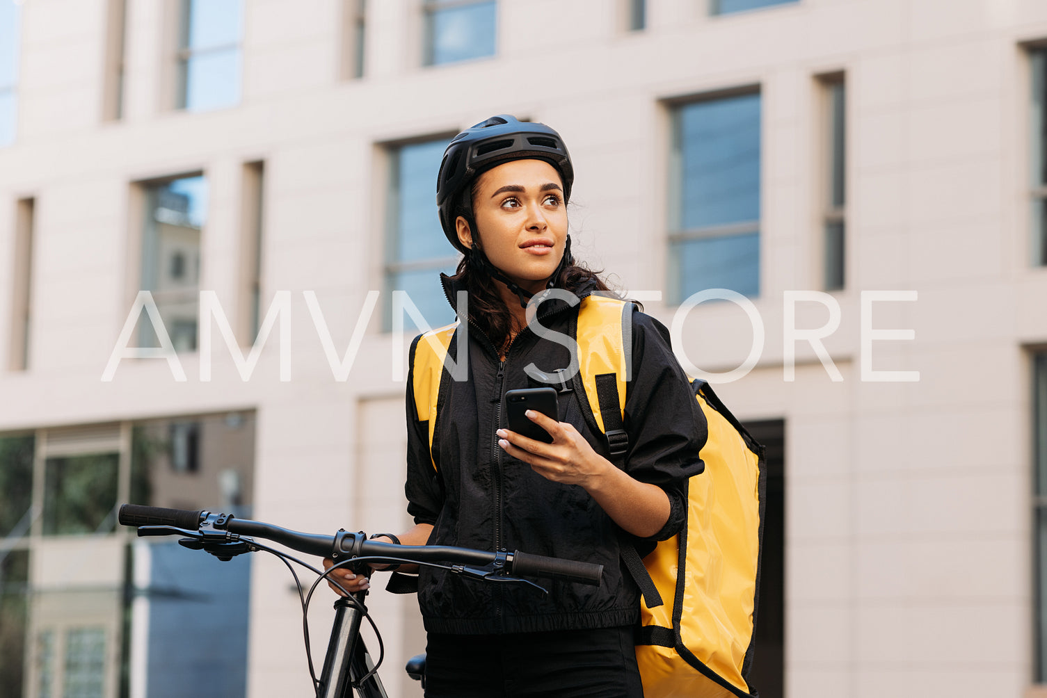 Young woman working for a delivery company standing in the city with a smartphone. Female with a yellow delivery backpack looking for the right address.