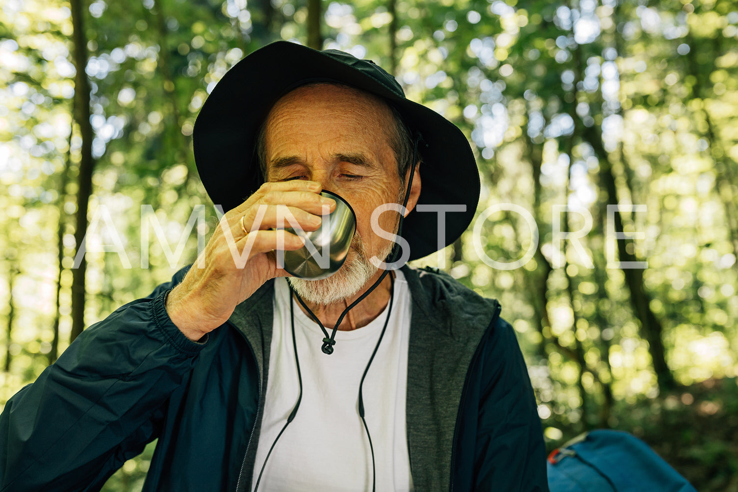 Senior male in hat drinking during his outdoor walk in forest