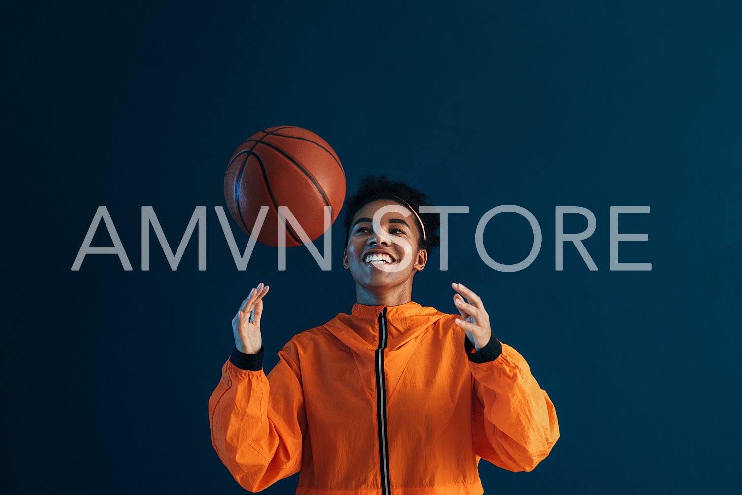 Smiling woman playing with a basketball in studio. Cheerful female practicing with a basketball against blue background.