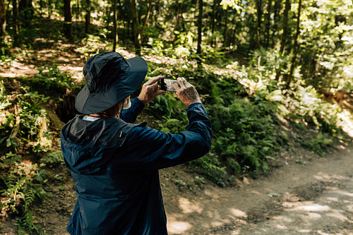 Back view of a male senior tourist taking photographs on his mobile phone during first walk