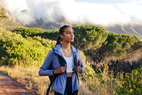 Young woman with backpack standing outdoors and watching sunset