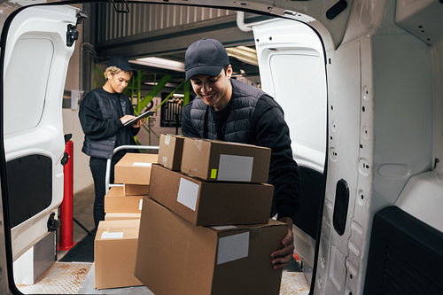 Smiling male courier loads cardboard boxes from a cart into the