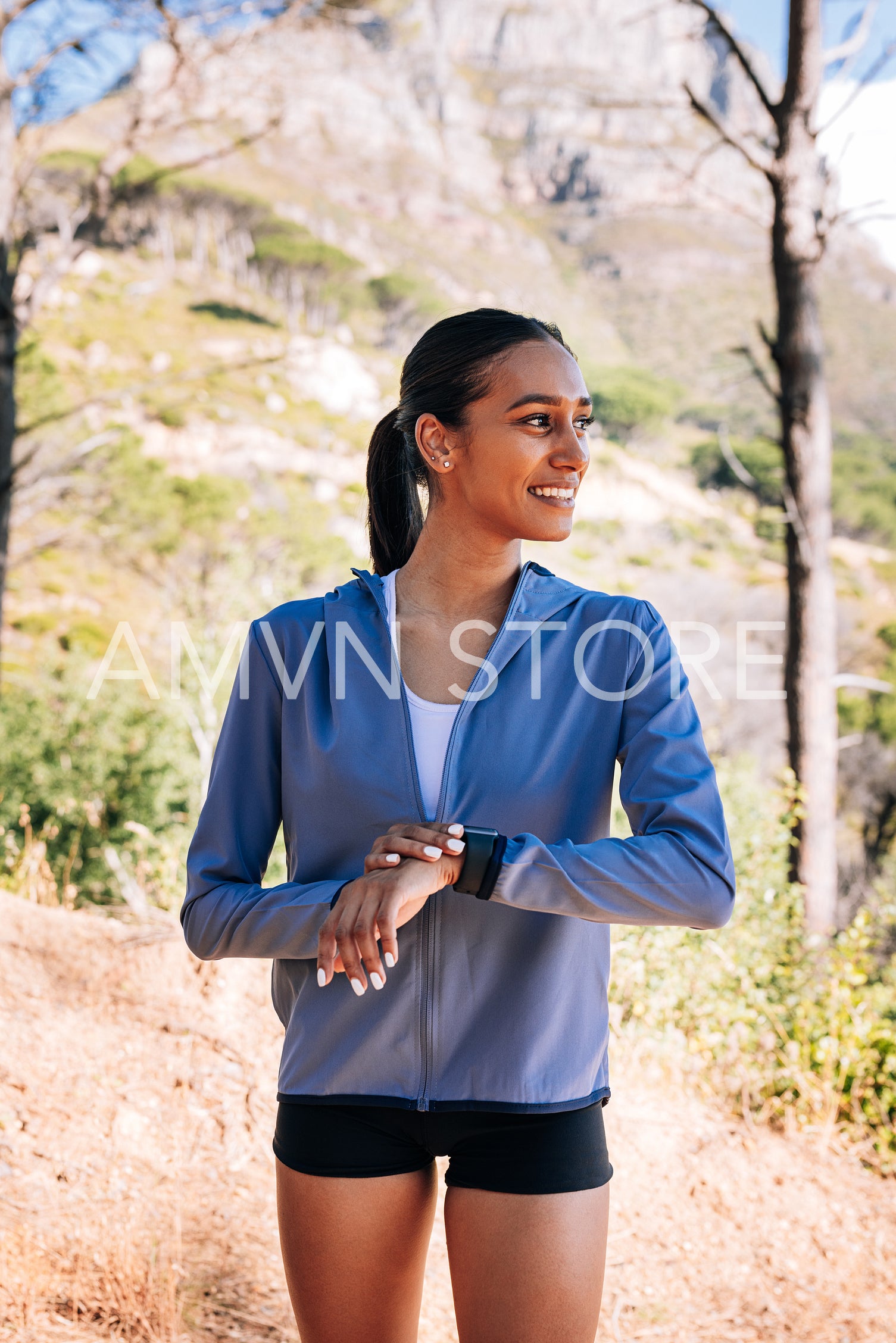 Side view of cheerful woman athlete looking away. Smiling female checking smartwatch outdoors.