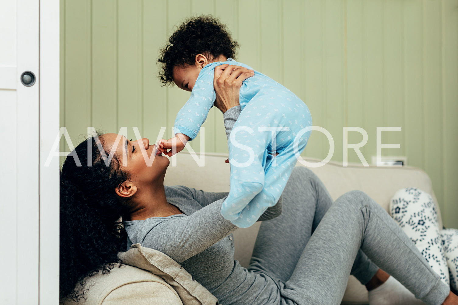 Side view of mother lifting baby in the air while lying on a sofa	