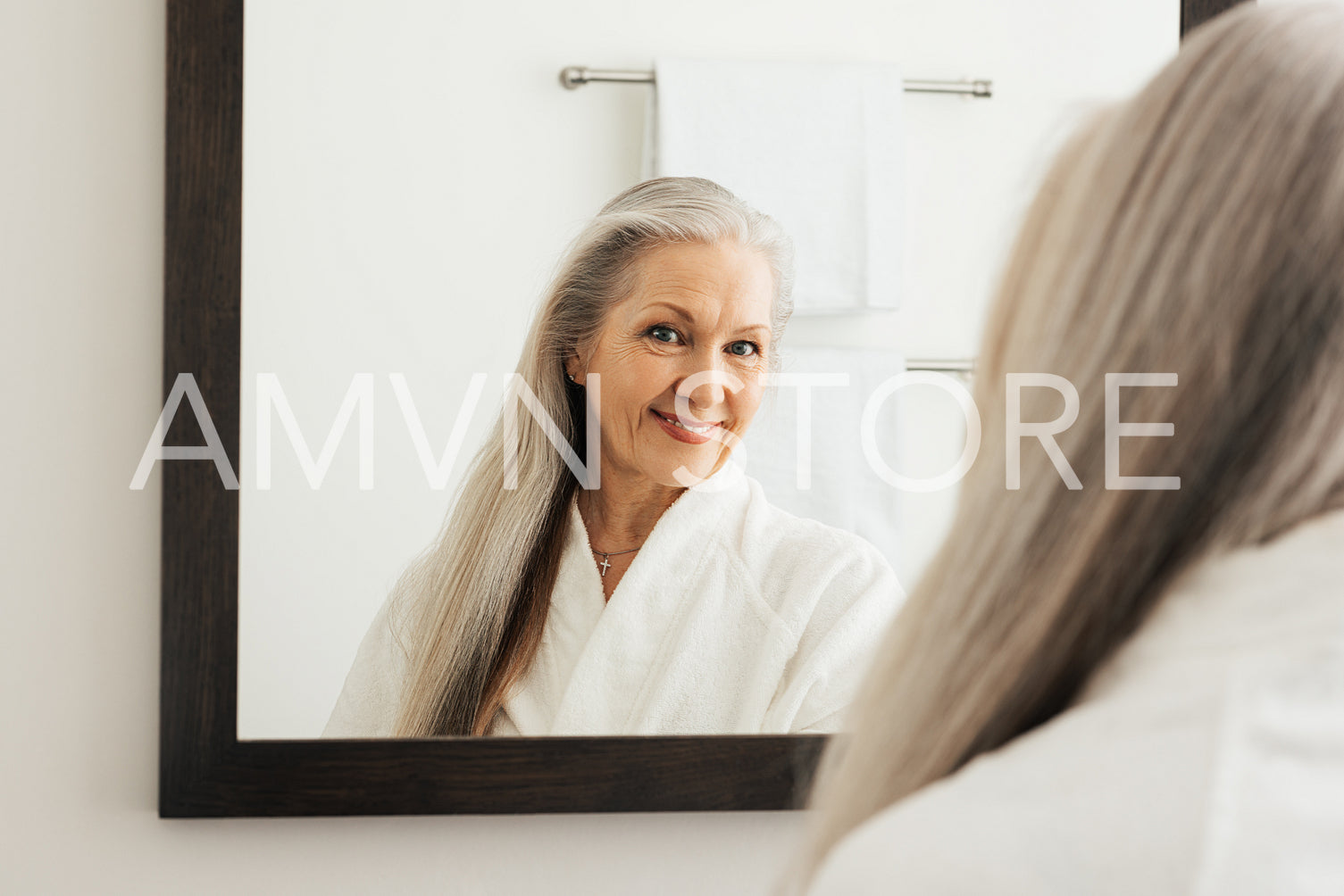 Older woman with long beautiful hair admiring herself in a mirror. Senior female in a bathroom in morning.