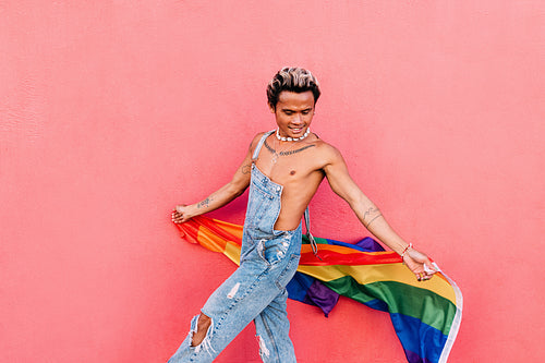 Young guy in denim overalls having fun holding rainbow LGBT flag