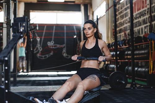 Muscular female using rowing machine in fitness club, front view