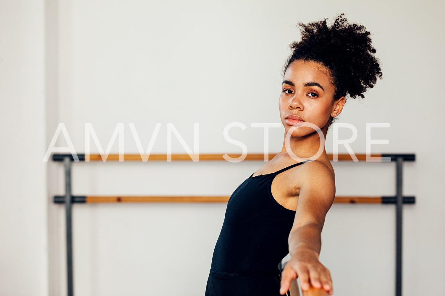 Portrait of a young ballerina relaxing at barre in dance studio and looking at camera	