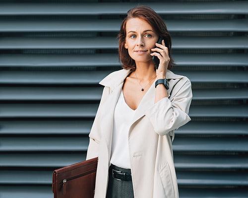 Middle-aged businesswoman talking on a mobile phone. Stylish business female with ginger hair standing outdoors.