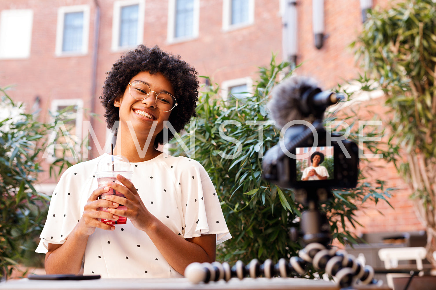 Happy woman recording a video on dslr camera, holding a juice	