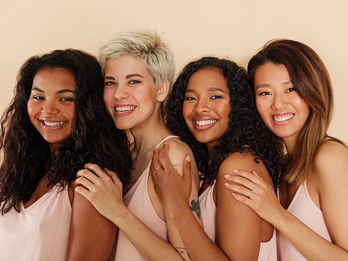 Group of smiling females standing together. Four women of different body types and skin tones looking at camera.