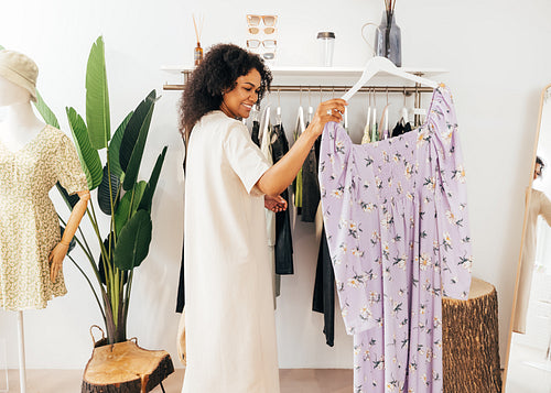 Woman choosing a dress. Side view of young stylish female standing near rack with hanger.