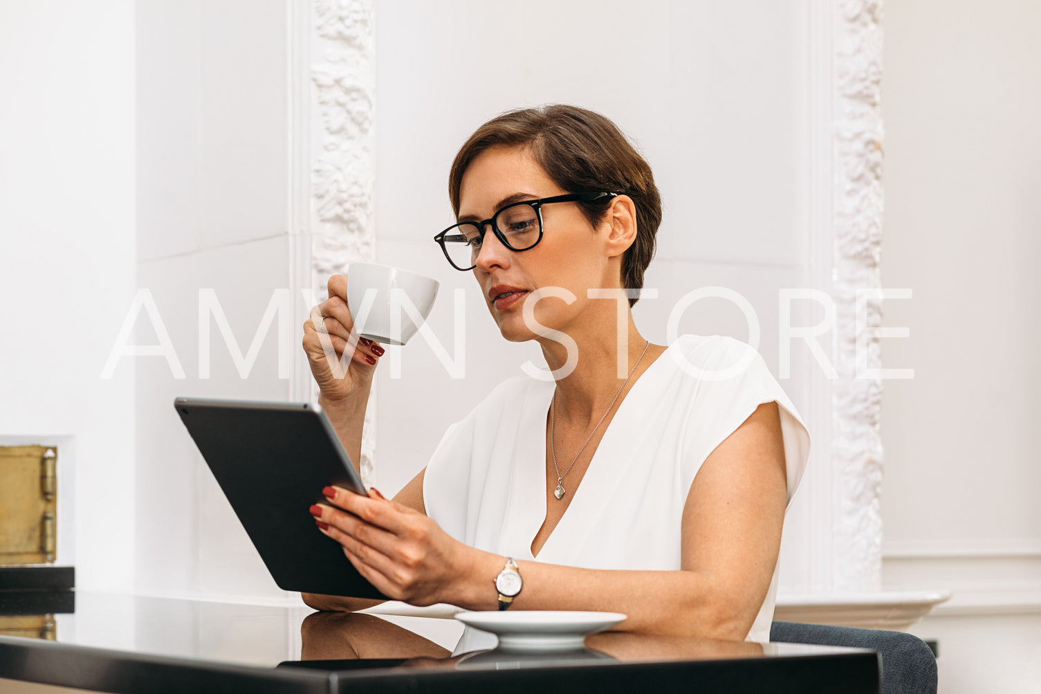 Mid adult woman holding a cup and looking on digital tablet. Businesswoman reading while having breakfast.	