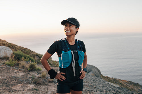 Portrait of a young woman in hiking attire standing in wild terrain and looking away at sunset