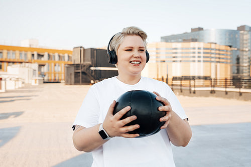 Portrait of a smiling healthy woman holding a medicine ball and standing on a roof