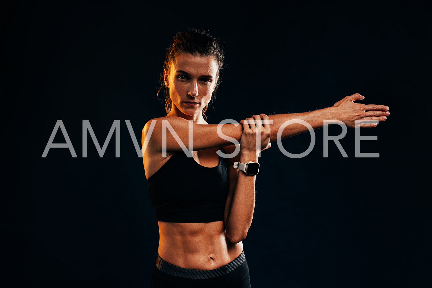 Female athlete in sportswear doing warm up exercise on black background