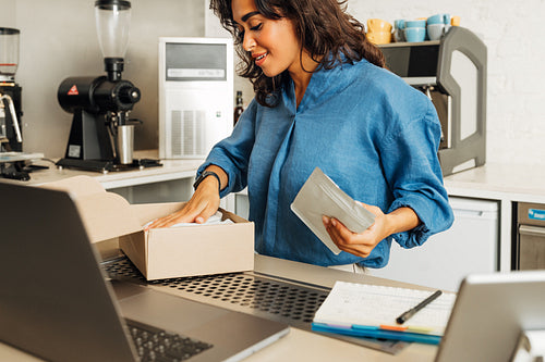 Young business owner puts a pack of coffee into cardboard box for shipment. Coffee shop owner preparing online order.