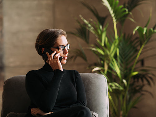 Serious and confident businesswoman in black formal wear looking away while sitting and talking on mobile phone