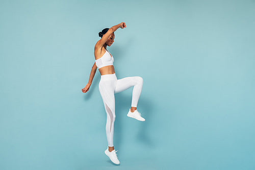 Sports woman jumping over blue background, warming up