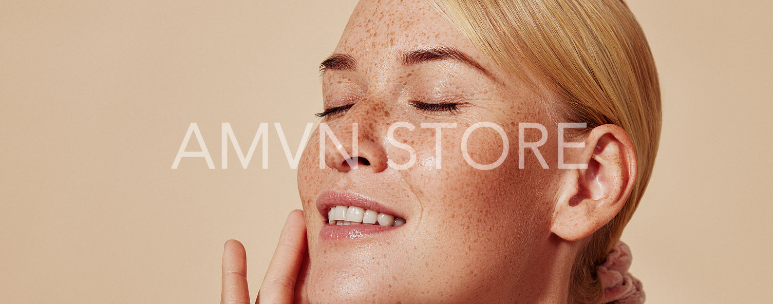 Side view of smiling blond woman with freckles touching her face. Close-up studio shot of young positive female with closed eyes against pastel background.