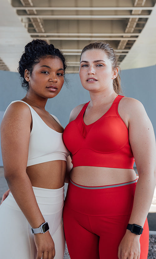 Portrait of two women in fitness attire with different colors looking at camera while standing outdoors