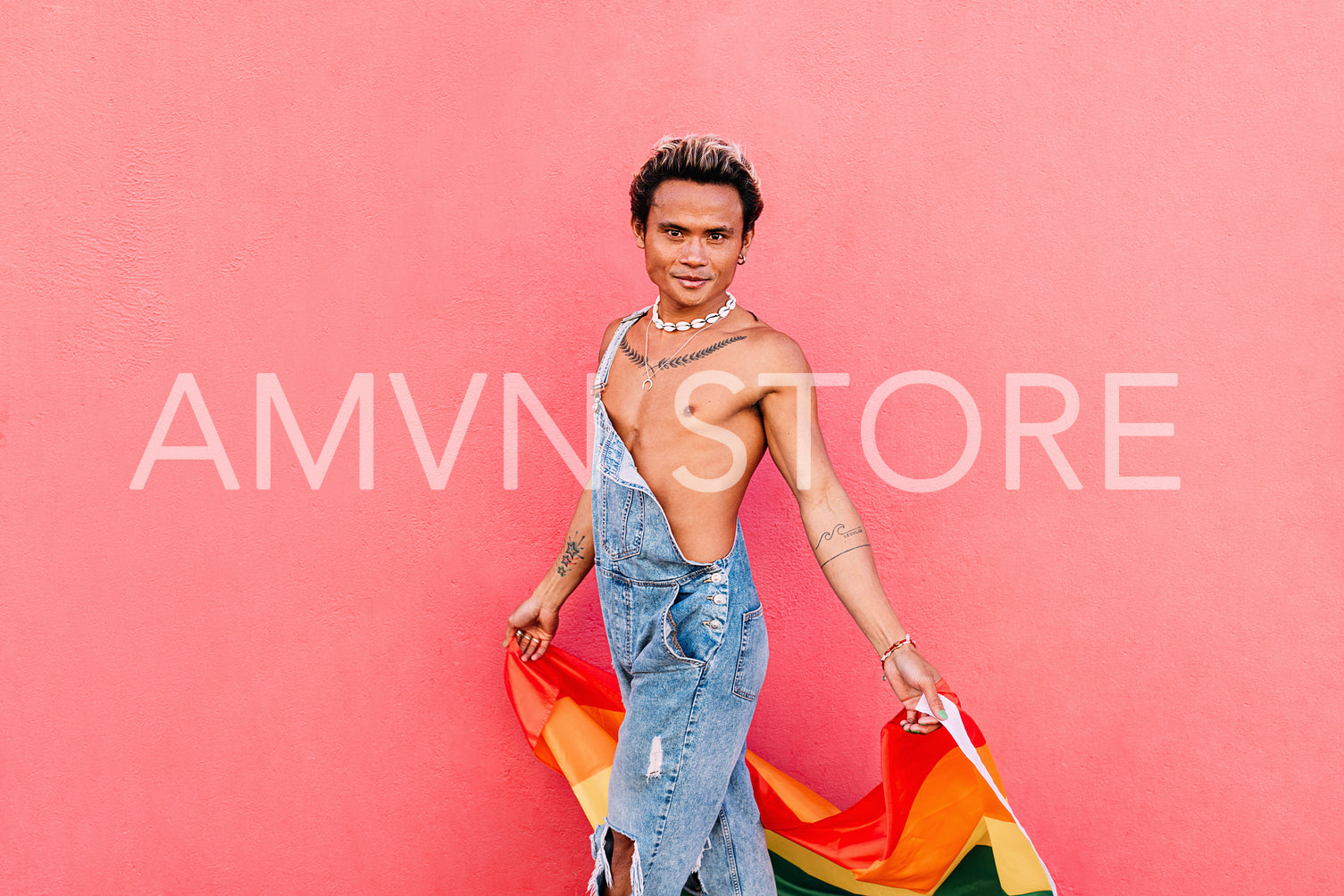 Young man walking with rainbow flag against pink wall