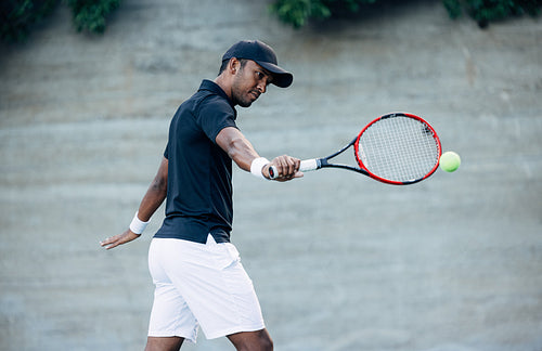 Young tennis player in cap hitting the ball during match outdoors