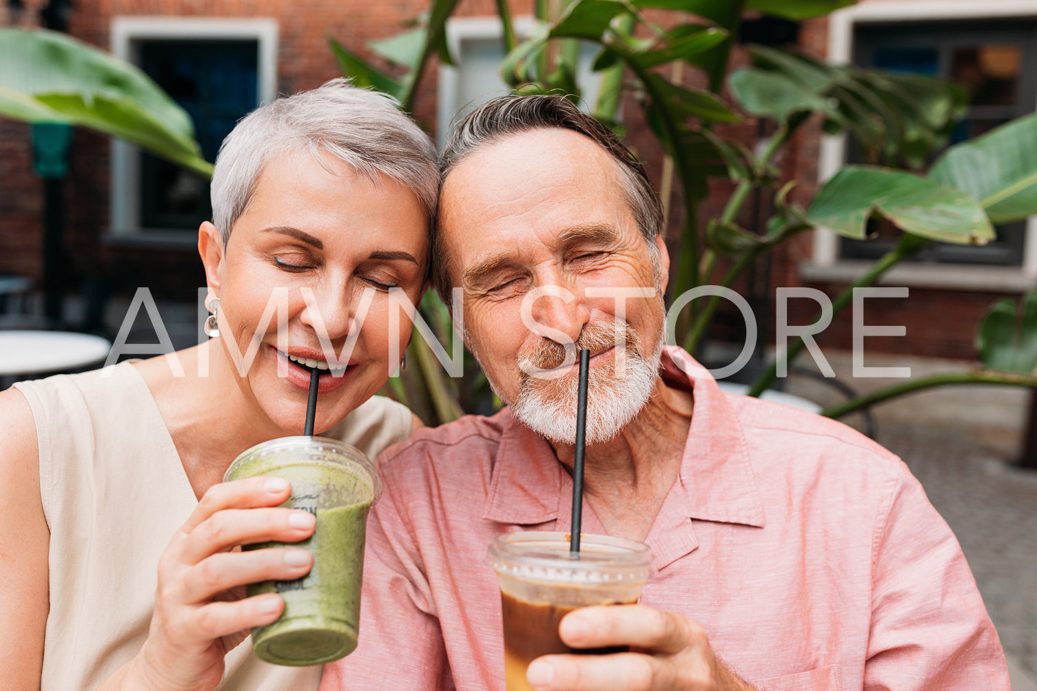 Aged smiling couple enjoying smoothies outdoors. Senior couple drinking cocktails together with closed eyes.