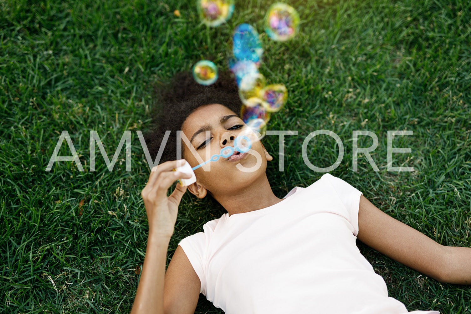 Girl lying on grass blowing bubbles in the air	