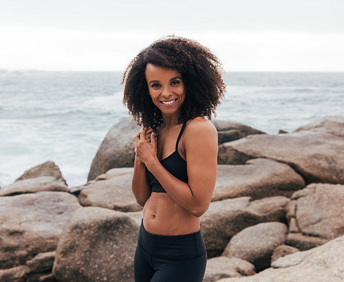 Happy female in sportswear standing outdoors at the coastline after exercises