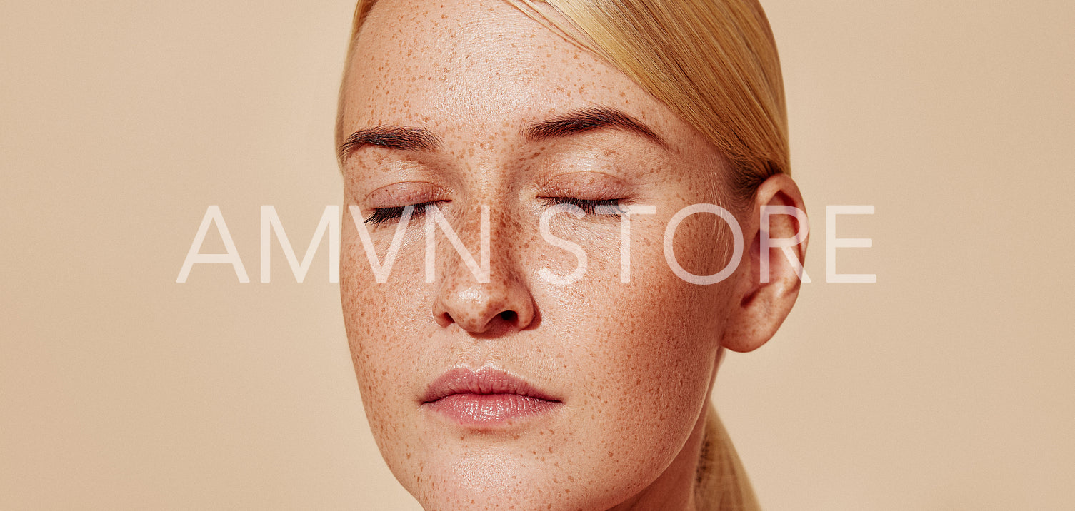 Close-up studio shot of a young beautiful blond woman with freckles. Cropped shot of female with smooth skin.