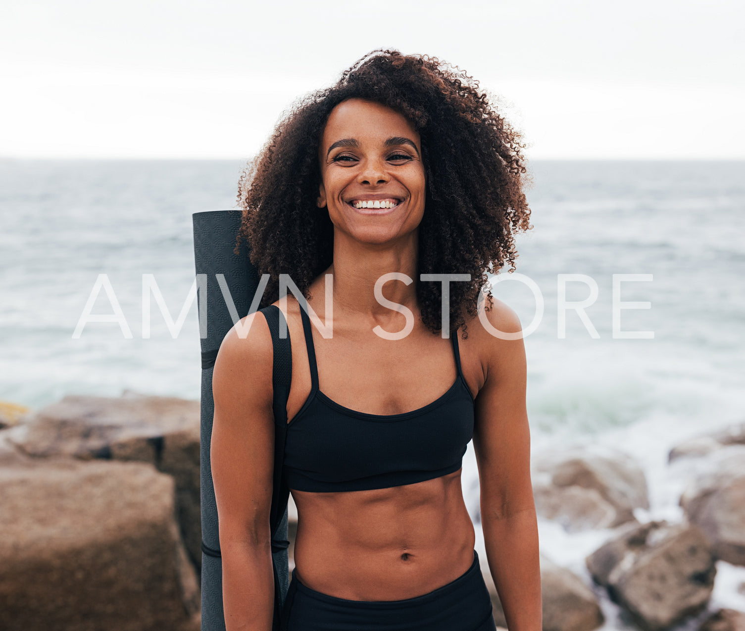 Muscular woman with yoga mat laughing while standing by ocean 