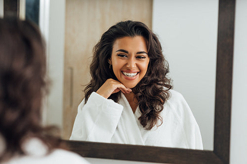 Reflection of happy woman in the mirror wearing white bathrobe