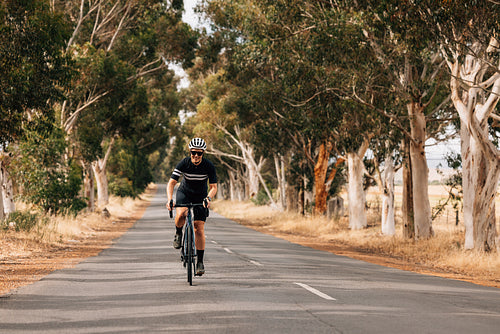 Smiling woman in sportswear riding her bike on empty countryside road