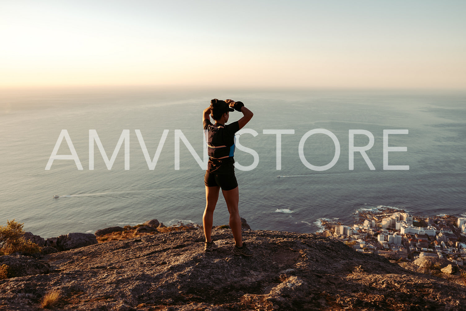 Rear view of young woman looking on the ocean from mountain top after hike