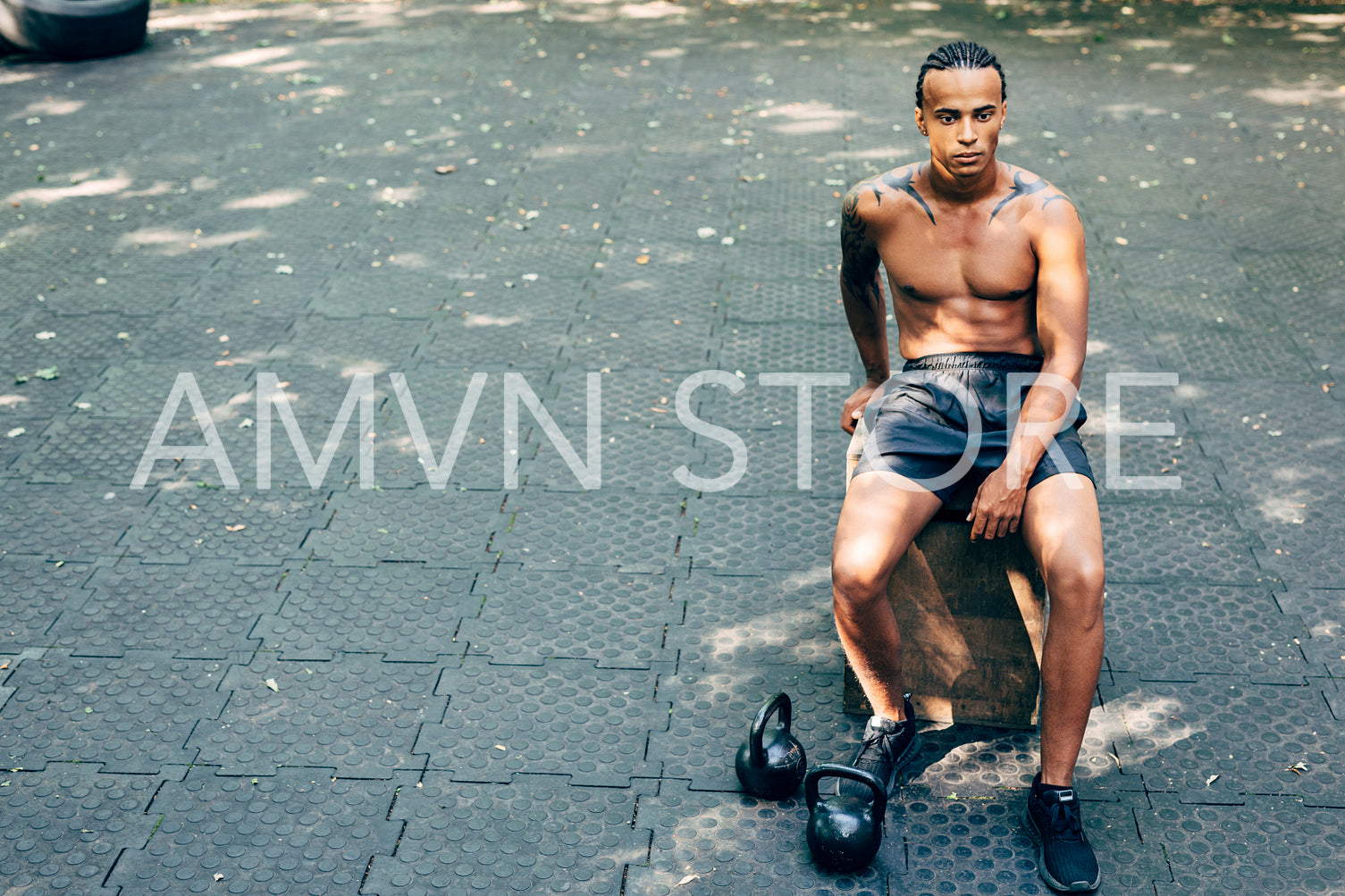 Bare chested man sitting outdoors during workout with kettlebells on the floor	