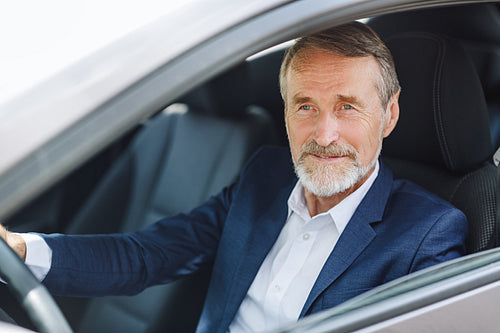 Senior driver sitting inside a car wearing formal wear