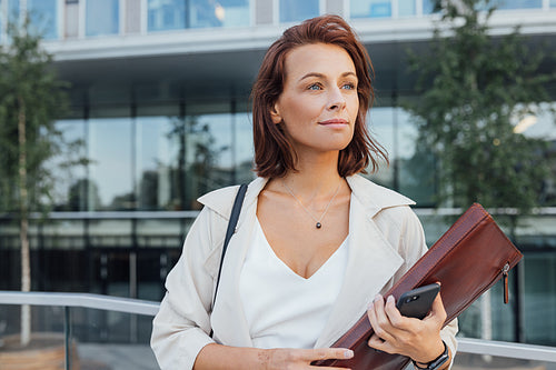 Middle-aged businesswoman outdoors. Female in formal wear and a leather folder looking away.