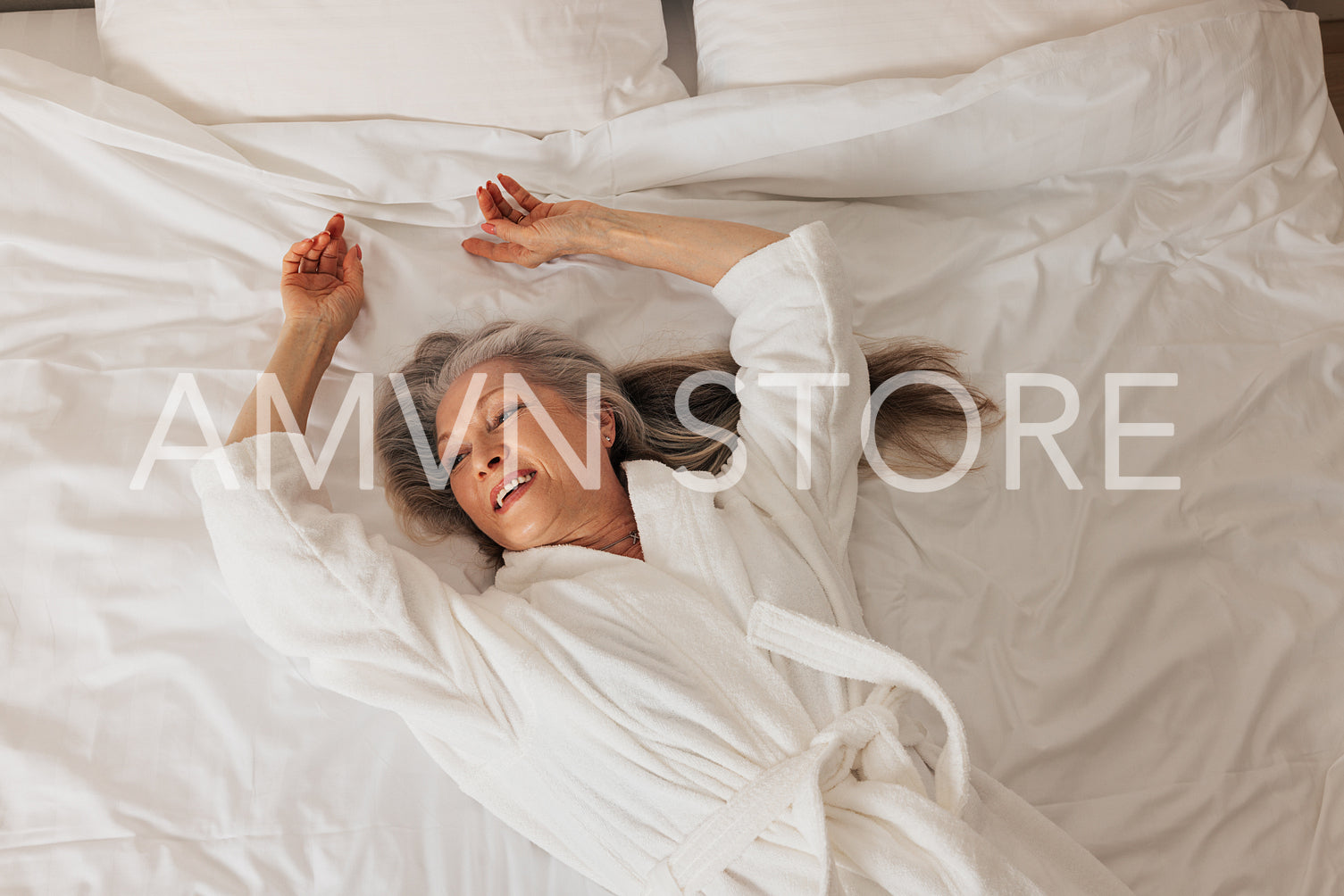 Smiling senior woman in a bathrobe lying on a bed and looking away. Female relaxing in a hotel room.