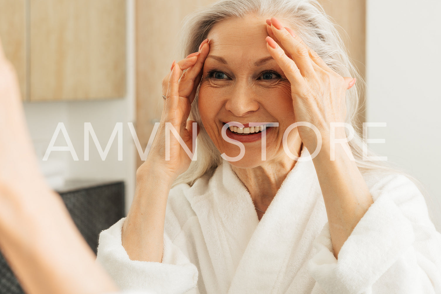 Close up of a happy aged woman touching her face with hands and looking at mirror