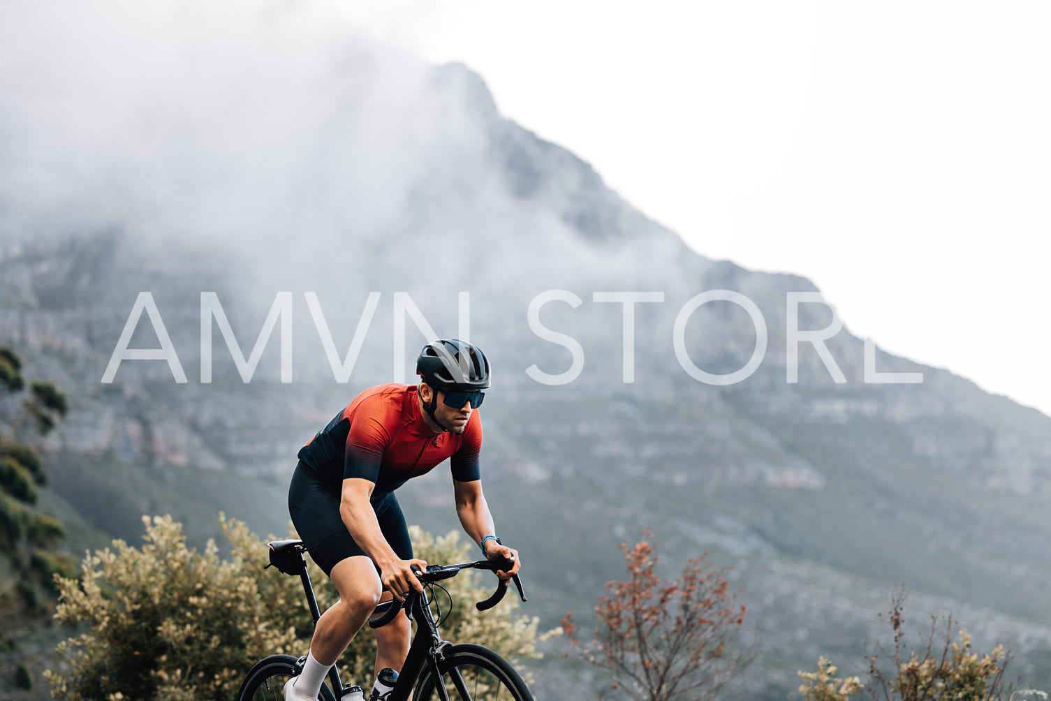 Professional male road bike rider exercising outdoors against the mountain with clouds