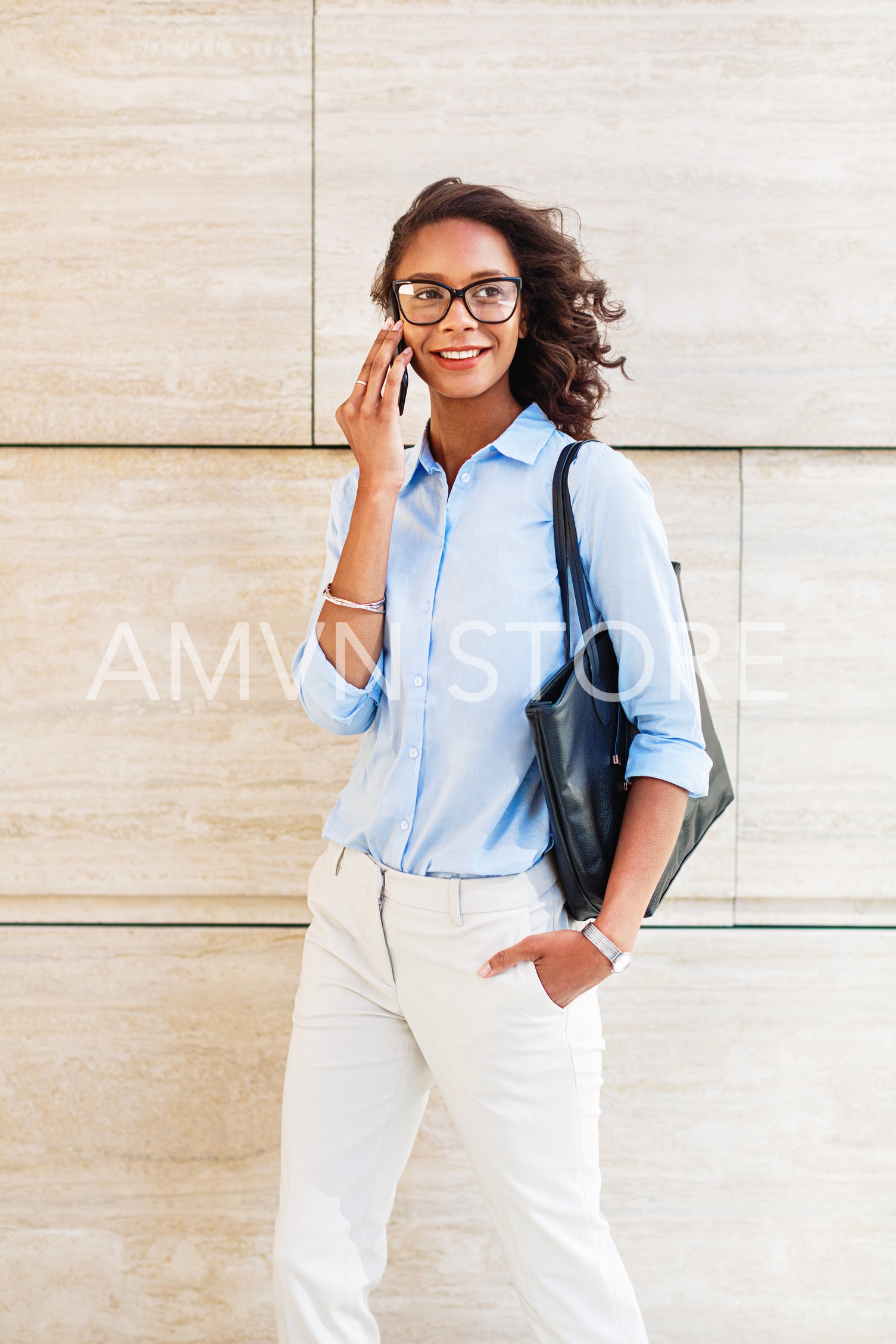 Smiling woman making phone call while standing at wall	