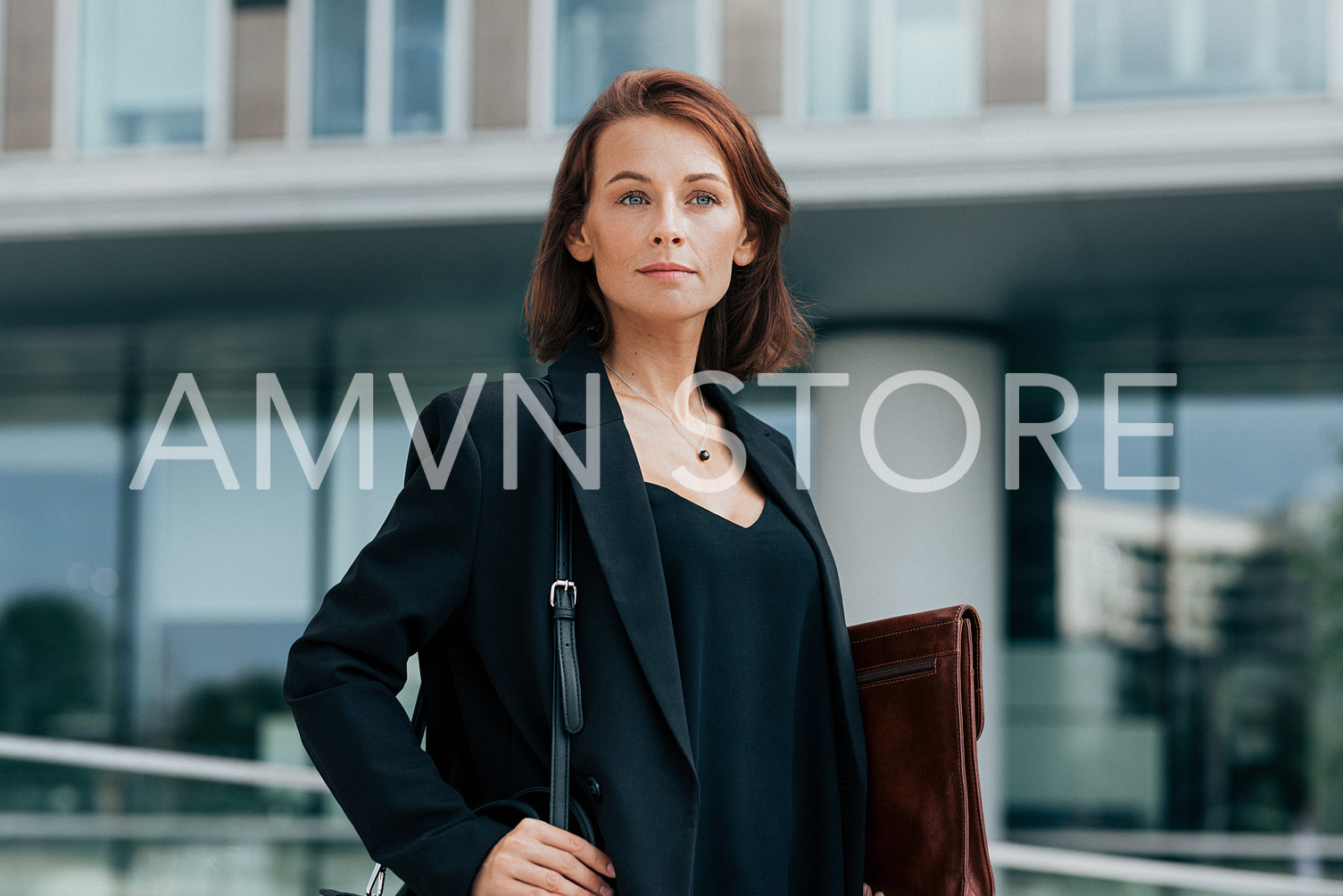 Confident middle-aged business woman with bag and leather folder standing against office building