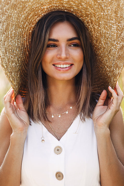 Beautiful cheerful woman hiding in her hat while standing outdoors