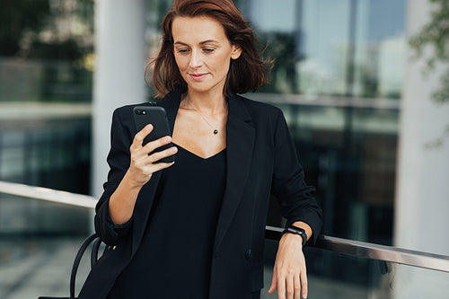 Confident middle-aged businesswoman standing outdoors and looking at a smartphone